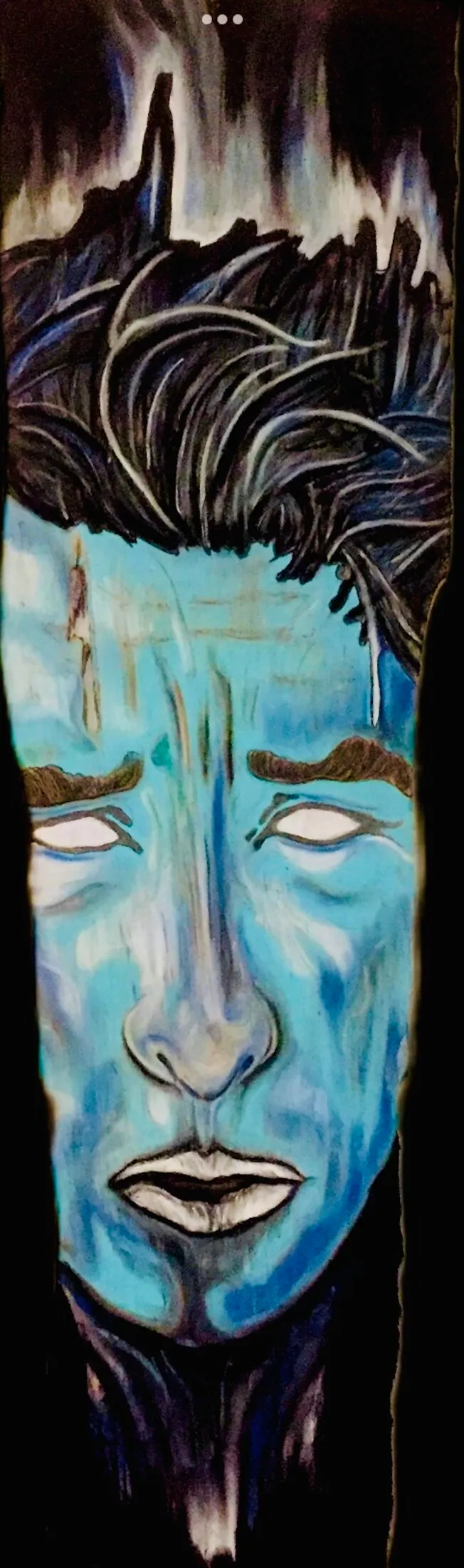 Close-up portrait of a face painted in blue and black tones. Dark, tousled hair with white streak highlights covers the top of the head; the face is rendered in light blue with visible eyes, nose and mouth, fading into black at the bottom of the canvas.
