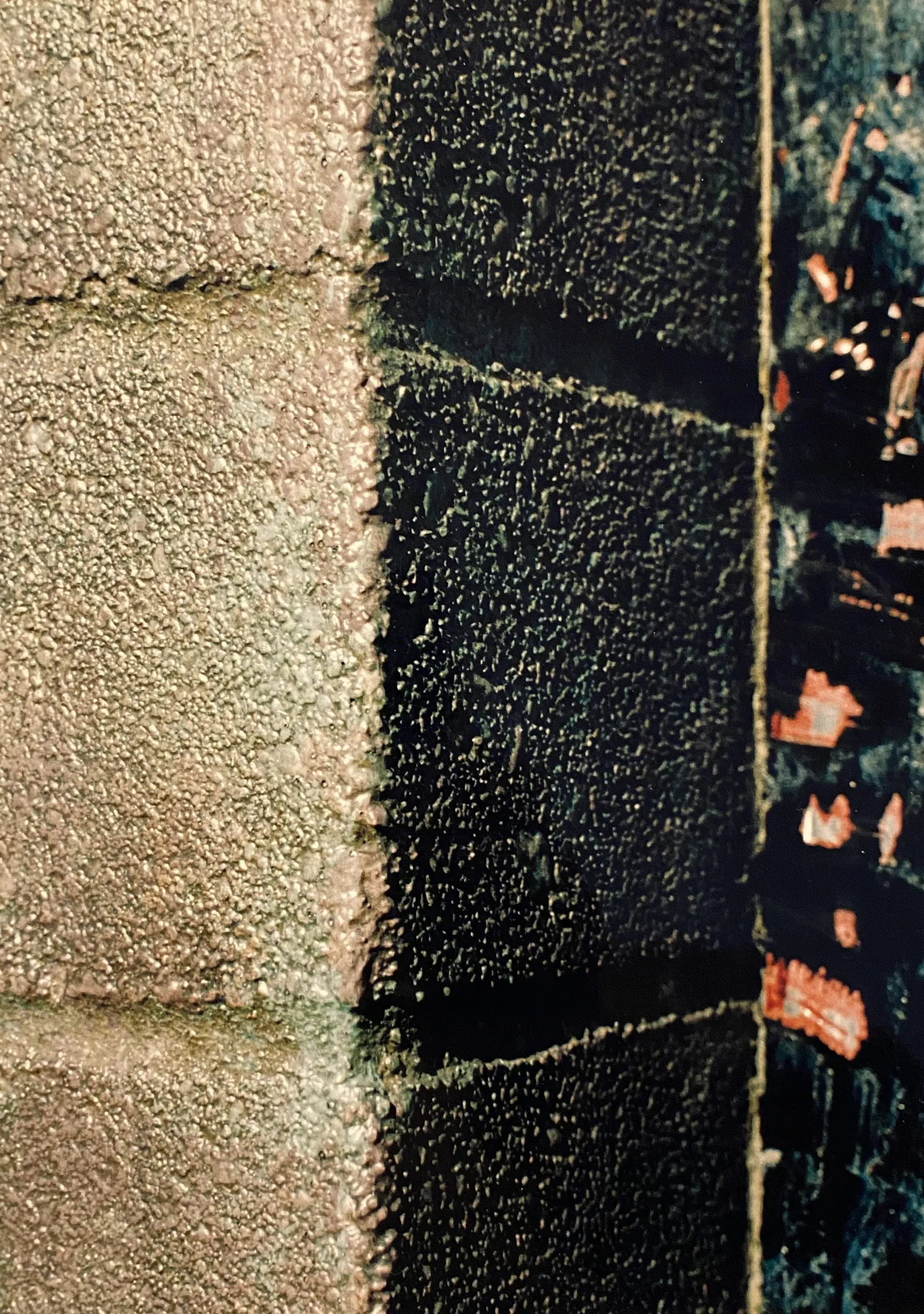 Close-up color photograph of a weathered concrete block wall, with lighter tan blocks on one side and darker, more textured blocks streaked with rust-orange marks on the other.