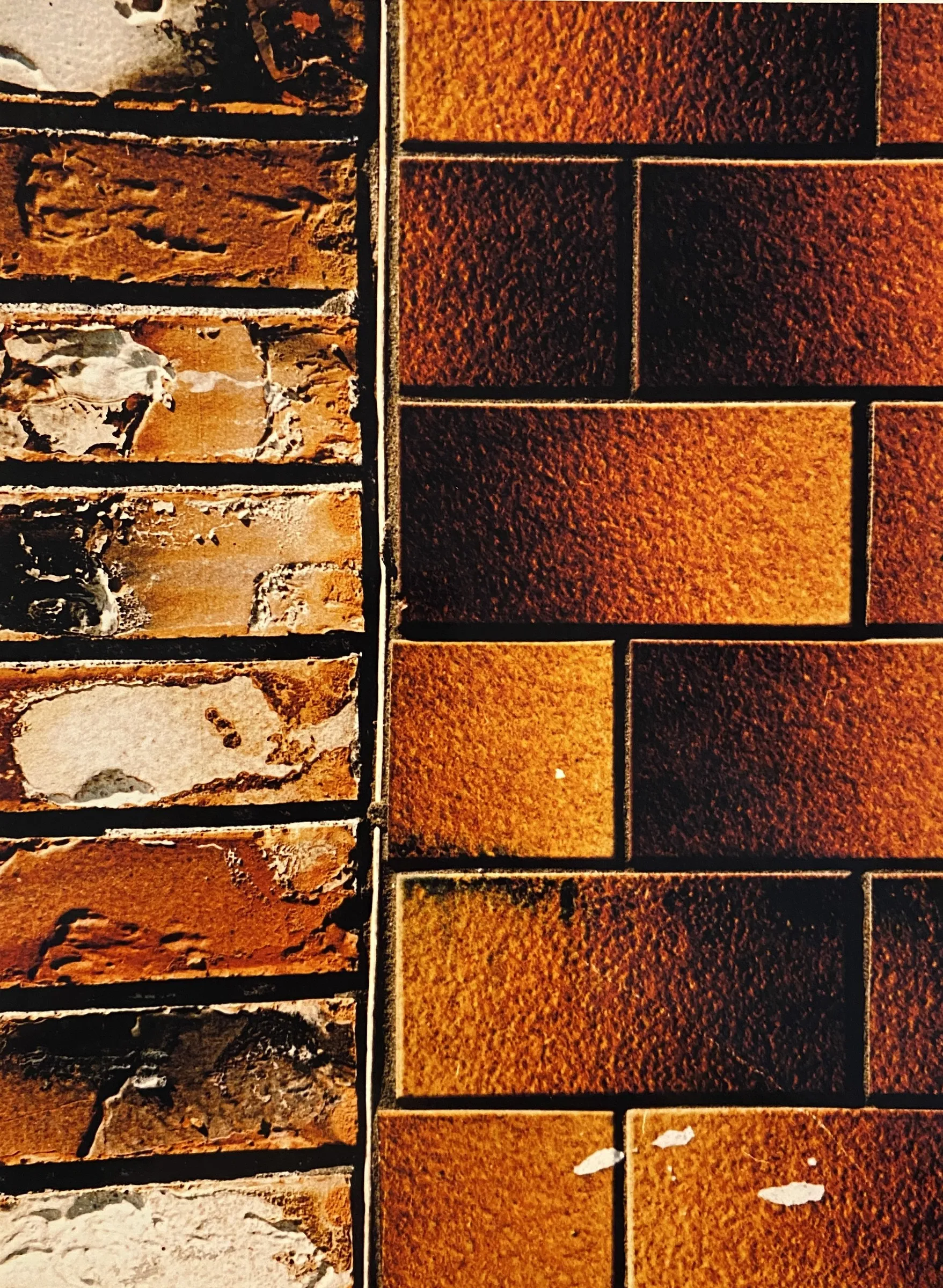 Close-up color photograph of a wall with weathered orange brick on the left and glazed amber and dark brown rectangular tile on the right, meeting at a vertical seam.